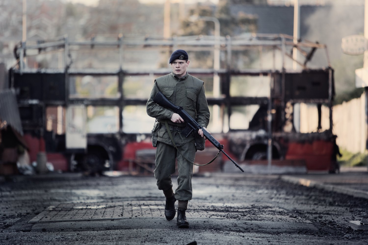Gary Hook katonai felszerelésben, fegyverrel, Belfast utcáin egy kiégett busz előtt